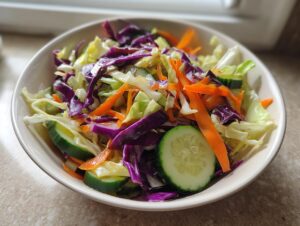 Close-up of a vibrant cabbage salad featuring shredded green and purple cabbage, carrots, and cucumber slices.