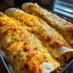 Close-up of three baked chicken enchiladas covered in melted, bubbly orange and white cheese and sprinkled with herbs.