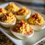Close-up of creamy, piped deviled eggs topped with bright red paprika on a white serving platter.