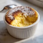 A golden brown baked egg custard, dusted with powdered sugar, served in a white ramekin.