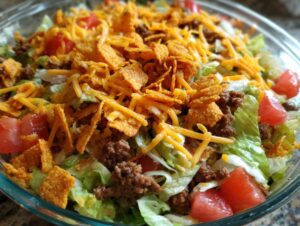 Close-up image of a vibrant taco salad featuring lettuce, seasoned ground beef, tomatoes, shredded cheese, and crunchy corn chips.