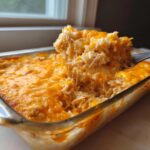 A spoonful of cheesy, creamy angel chicken rice casserole being lifted from a glass baking dish.