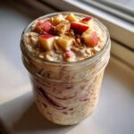 Close-up of apple cinnamon overnight oats in a mason jar, topped with diced red apples and cinnamon.