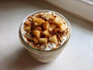 Overhead view of apple cinnamon overnight oats topped with diced apples and cinnamon in a glass jar.