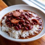 A close-up of authentic red beans and rice topped with slices of smoked sausage in a white bowl.