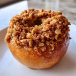 Close-up of a single, glistening baked apples topped generously with a brown sugar and oat crumble.