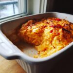 A scoop taken out of hot, cheesy Buffalo chicken dip baked in a white rectangular casserole dish.