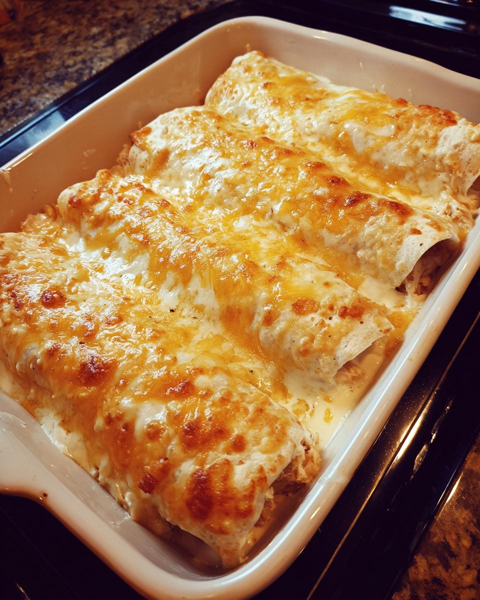 Three rolled chicken enchiladas covered in bubbling, melted, golden-brown cheese in a white baking dish.