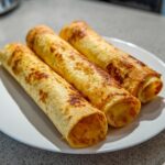 Three golden-brown Baked Cream Cheese Chicken Taquitos rolled tightly on a white plate.