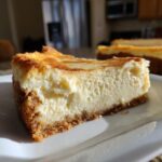 A thick slice of creamy baked cheesecake with a golden top and graham cracker crust, representing the banana cream cheesecake.