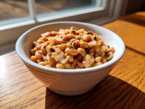 A white bowl filled with cooked black eyed peas recipe, garnished with diced onions, sitting on a sunlit wooden table.