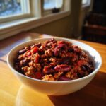 A close-up of a white bowl filled with rich, chunky high protein chili featuring ground meat and dark red kidney beans.