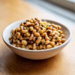 A close-up of a white bowl filled with savory, seasoned black eyed peas recipe ingredients.