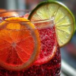 Close-up of a glass filled with bubbly, deep red non-alcoholic christmas punch garnished with orange and lime slices.