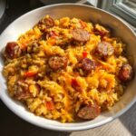 Close-up of cheesy sausage and rice mixture topped with melted cheddar cheese and sliced smoked sausage.