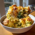 A spoonful of creamy chicken broccoli rice casserole with a golden, cheesy baked top being lifted from a white bowl.