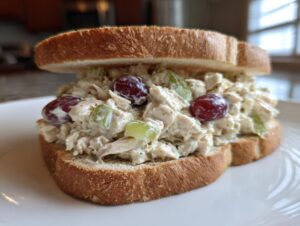 A thick, open-faced chicken salad sandwich featuring creamy filling with grapes and celery on toasted bread.