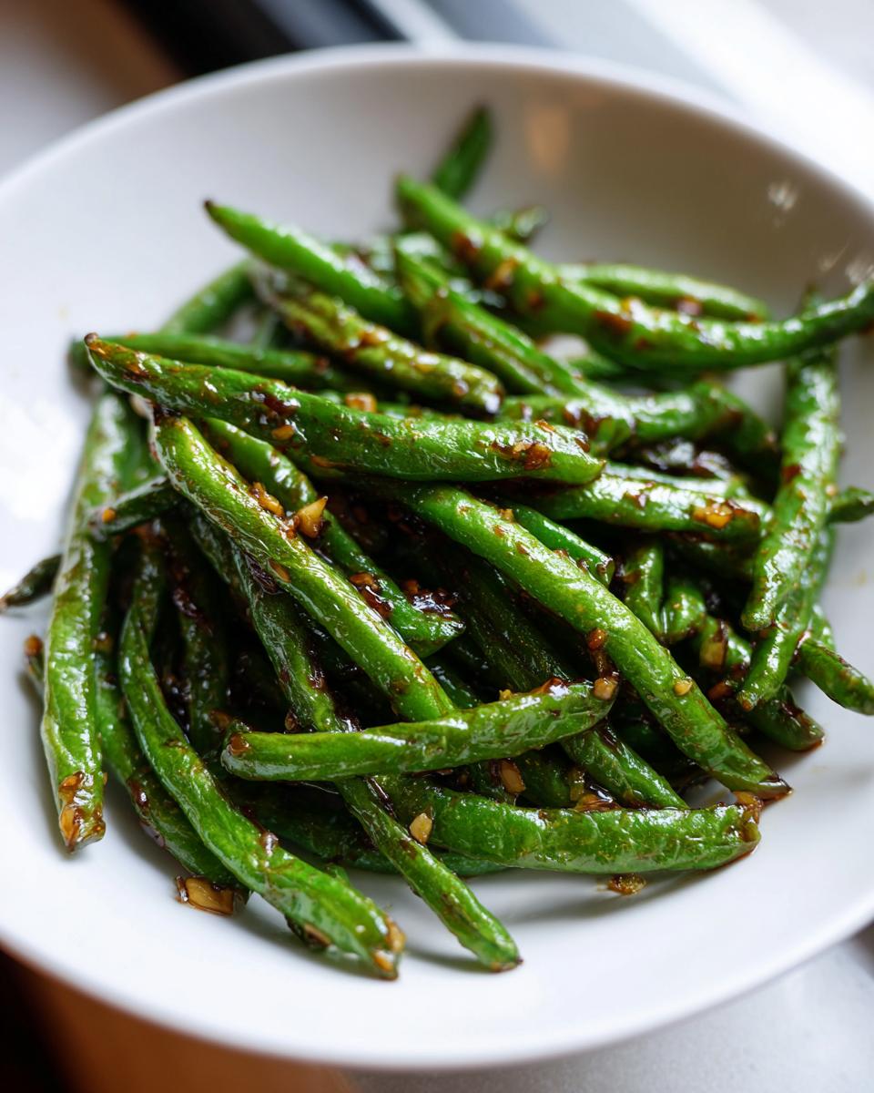 A close-up of vibrant, glossy chinese green beans with garlic sauce served in a white bowl.