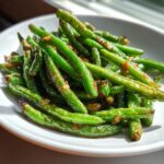 Close-up of bright green, blistered chinese green beans with garlic sauce piled in a white bowl.