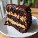 A decadent slice of chocolate peanut butter cake featuring dark layers and creamy peanut butter filling, topped with dripping chocolate ganache.