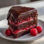 A decadent slice of chocolate raspberry cake featuring dark layers, bright raspberry filling, and rich chocolate ganache dripping down the side.