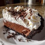 A decadent slice of Christmas chocolate cream pie featuring a thick chocolate layer and tall whipped cream topping with chocolate shavings.