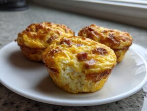 Three golden-brown cottage cheese egg cups, lightly browned on top with visible ham pieces, served on a white plate.