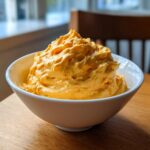 A creamy, bright orange mound of cottage cheese queso dip served in a white bowl on a wooden table.