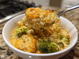 A spoonful of creamy chicken broccoli rice casserole lifted from a white bowl, showing cheesy sauce and tender chicken.