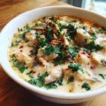 Close-up of a rich, creamy chicken and mushroom coconut soup topped with fresh cilantro and red pepper flakes.
