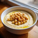 A white bowl filled with creamy chickpea soup, drizzled with olive oil and topped with whole spiced chickpeas.