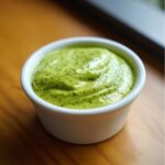 A close-up of thick, bright green cilantro lime sauce swirled in a small white dipping bowl.