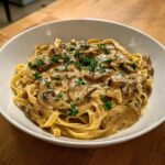 A close-up of creamy mushroom pasta with fettuccine noodles topped with fresh parsley.