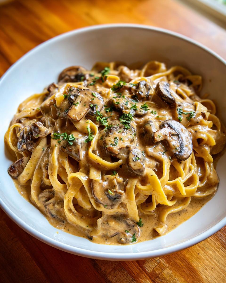 Close-up of creamy mushroom pasta with fettuccine noodles and sliced mushrooms, garnished with parsley.