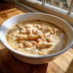 A close-up of a bowl of creamy white chicken chili featuring shredded white chicken and cannellini beans.