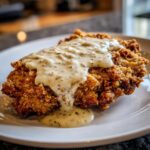 Close-up of a perfectly crispy chicken fried steak smothered in creamy, black pepper gravy on a white plate.