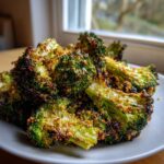 A close-up of perfectly cooked smashed broccoli florets, heavily coated and crispy, served on a white plate.
