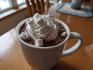 Close-up of a white mug filled with rich crockpot hot chocolate topped with whipped cream and marshmallows.