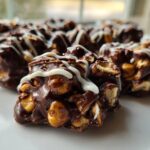 Close-up of several rich, chocolate crockpot peanut clusters drizzled with white chocolate on a white plate.