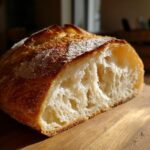 Close-up of a freshly baked french bread loaf cut in half, showing a crusty golden exterior and an airy, open crumb structure.