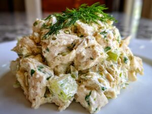 A close-up mound of creamy dill pickle chicken salad, garnished with fresh dill sprigs.