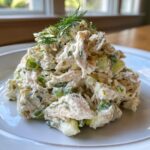 A close-up of a generous serving of creamy dill pickle chicken salad garnished with fresh dill.