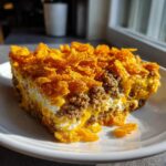 A close-up slice of Dorito Casserole featuring layers of ground meat, creamy sauce, and a crunchy orange Dorito topping.