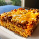 A close-up, appetizing slice of doritos casserole with ground beef, topped with melted cheddar and Monterey Jack cheese.