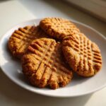 Four golden brown Easy Peanut Butter Cookies with classic criss-cross fork marks on a white plate.
