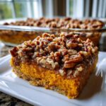 A close-up of a slice of easy sweet potato casserole featuring a bright orange base and a thick, crunchy pecan crumble topping.