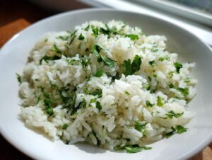 A close-up of fluffy white cilantro lime rice mixed with fresh chopped cilantro in a white bowl.