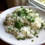 A close-up of fluffy cilantro lime rice topped with fresh cilantro leaves served in a white bowl.