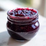 Close-up of a small glass jar filled with rich, dark purple homemade blackberry jam.