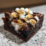 Close-up of a fudgy hot chocolate brownie square topped with toasted marshmallows and chocolate drizzle.
